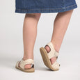Beige pretty brave sandals worn with a denim skirt on a plain background
