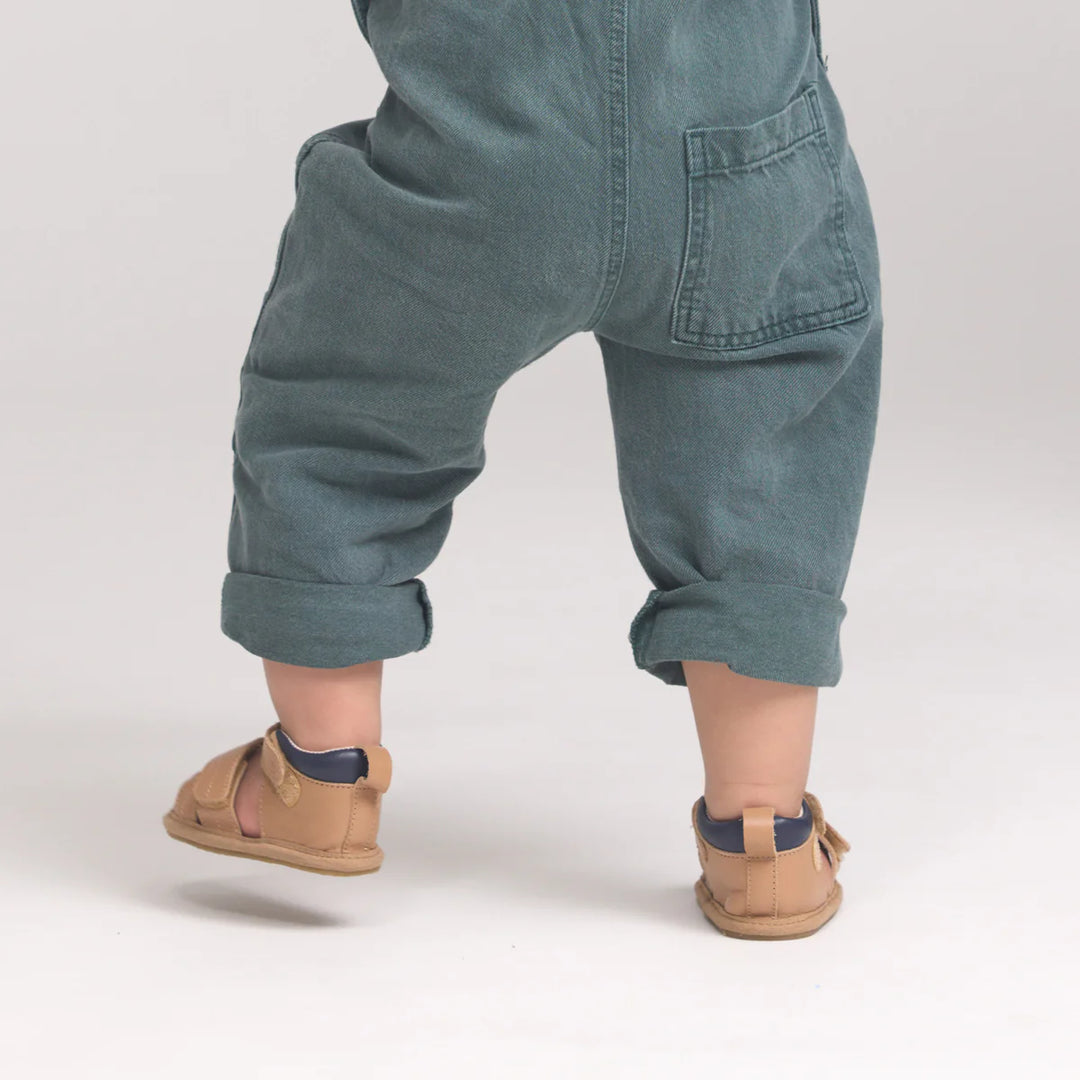 Child wearing blue denim overalls and tan sandals on a plain background