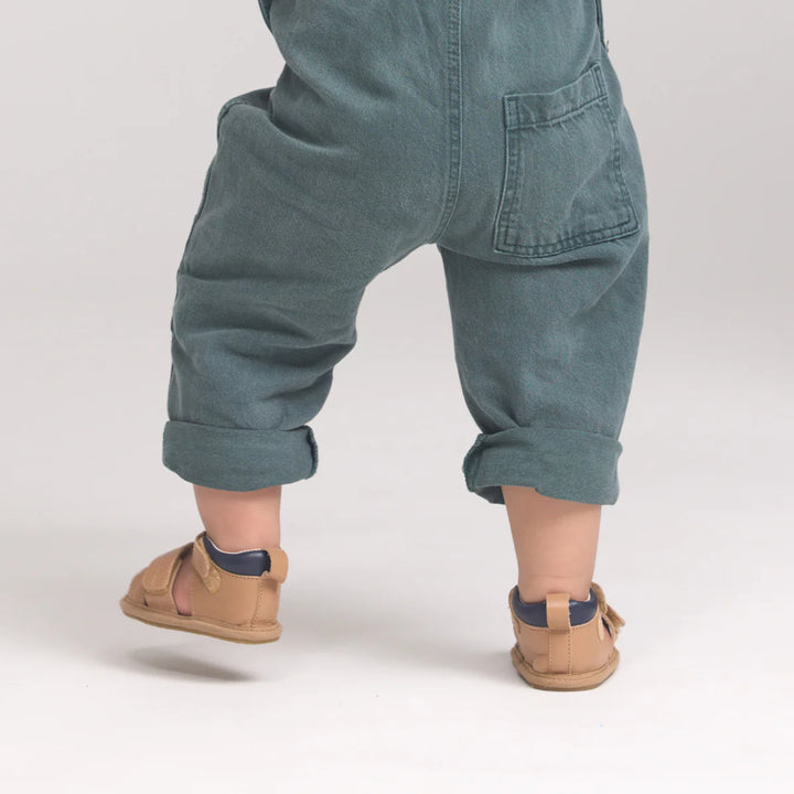 Child wearing blue denim overalls and tan sandals on a plain background