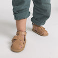 Child wearing brown pretty brave sandals on a plain background