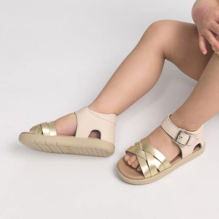 pretty Brave Beige sandals with gold accents worn by a person on a light gray background