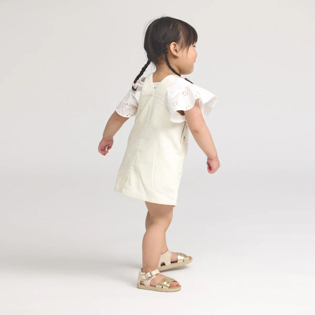 Young child wearing a white dress with ruffled sleeves on a plain background