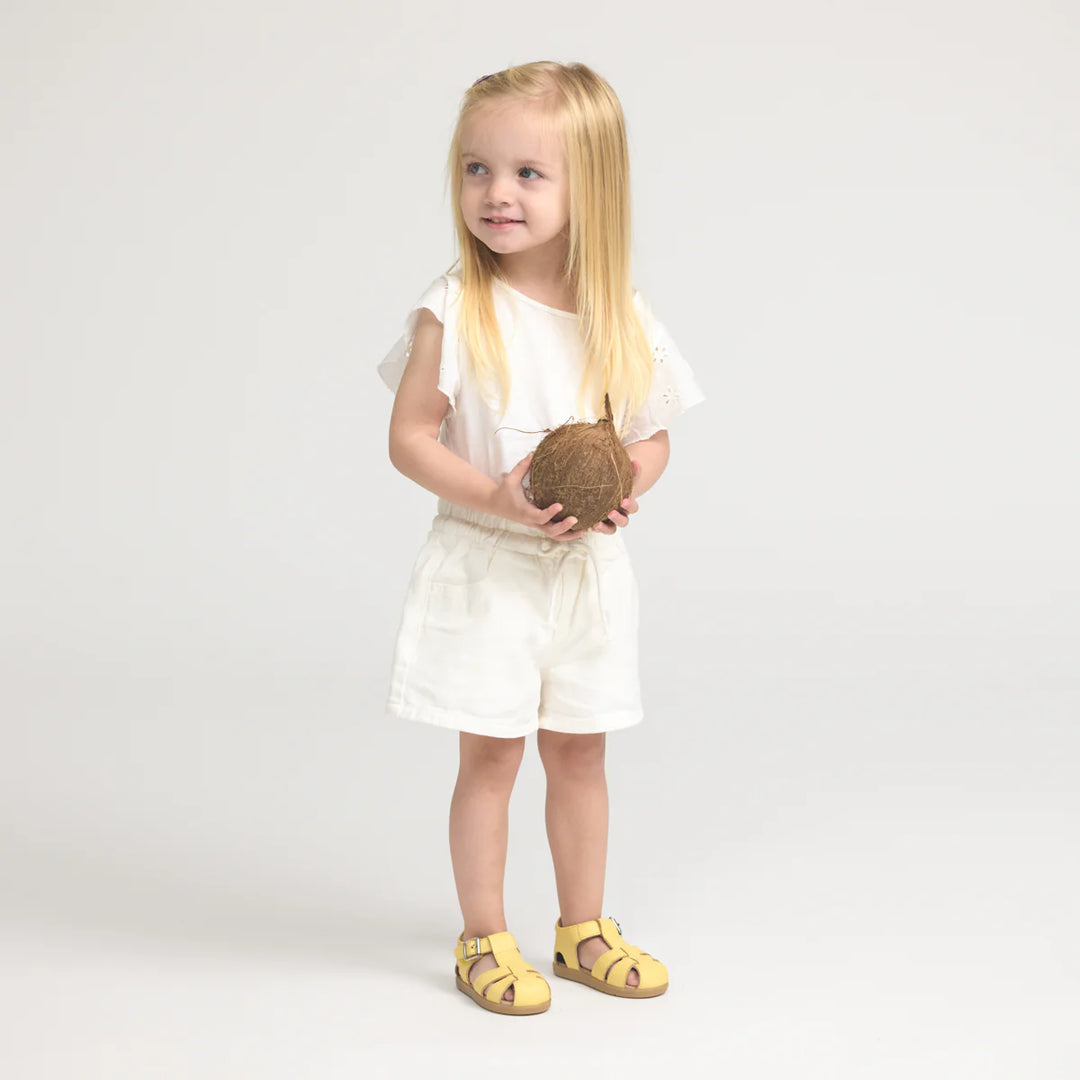 Young girl holding a coconut in a white dress on a light gray background