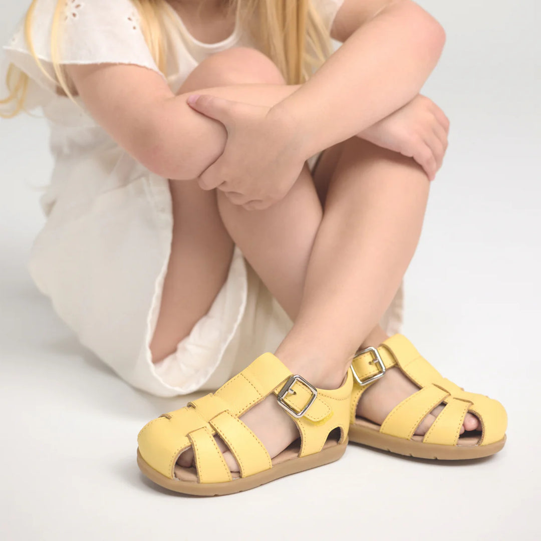Child wearing yellow pretty brave sandals on a light background