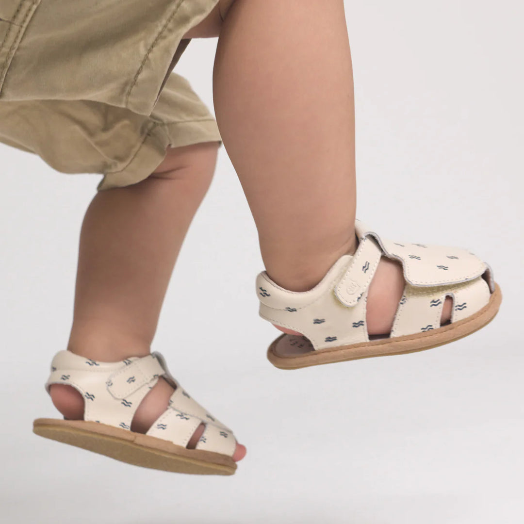 Child wearing cream pretty brave sandals with small black patterns on a light gray background