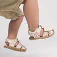 Child wearing cream pretty brave sandals with small black patterns on a light gray background