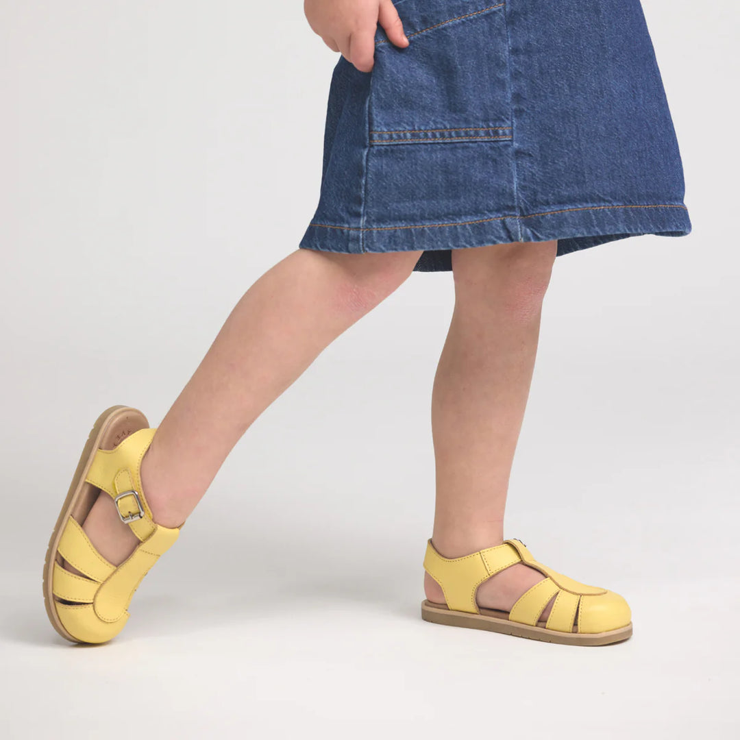 Person wearing yellow pretty brave sandals and a blue denim skirt on a light gray background