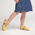 Person wearing yellow pretty brave sandals and a blue denim skirt on a light gray background