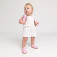 Baby in a white lace dress with pink pretty brave sandals on a plain background