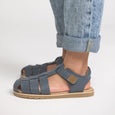 Pretty Brave Blue sandals worn with rolled-up jeans on a light gray background