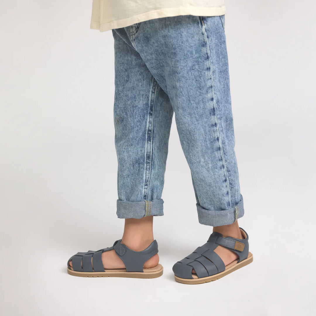 Child wearing blue jeans and pretty brave sandals on a plain background