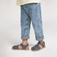 Child wearing blue jeans and pretty brave sandals on a plain background