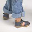 Child wearing pretty brave blue sandals with rolled-up jeans on a light background