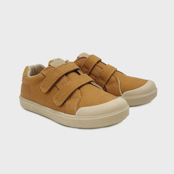 A pair of toddler's low-top canvas sneakers in a warm camel brown color, featuring two adjustable hook-and-loop straps and a light beige rubber sole and toe cap, shown against a light gray background.
