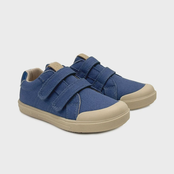A pair of blue canvas toddler sneakers with beige rubber toe caps and soles, featuring two hook-and-loop straps, shown on a light gray background.