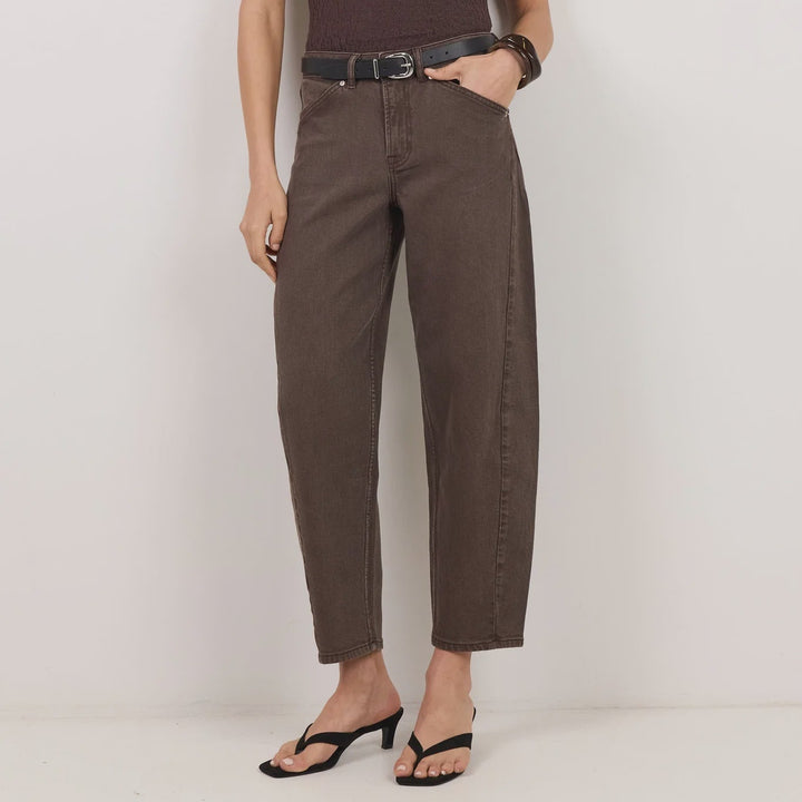 A woman modeling a dark brown short-sleeve top with a sheer lace yoke and high neck, paired with dark brown wide-leg cropped pants, a black belt, and black heeled sandals against a plain light gray studio background.