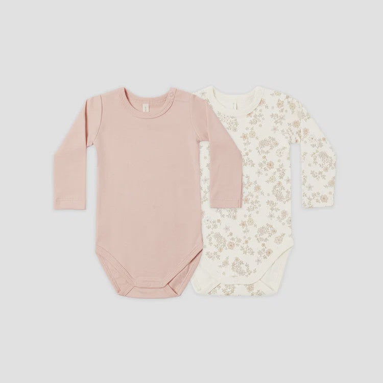 Two long-sleeve baby bodysuits laid flat on a light gray background. The front bodysuit is a solid dusty pink, and the back bodysuit is cream with a delicate beige floral pattern.