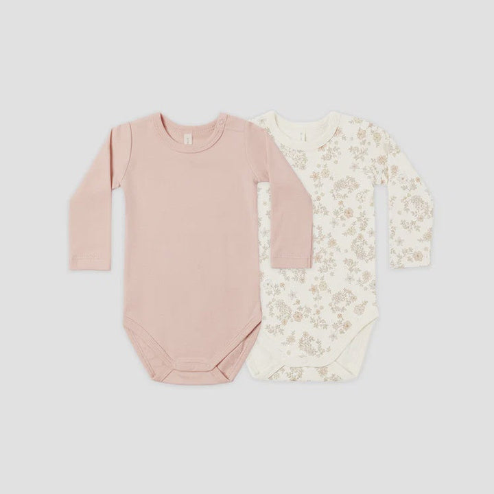 Two long-sleeve baby bodysuits laid flat on a light gray background. The front bodysuit is a solid dusty pink, and the back bodysuit is cream with a delicate beige floral pattern.