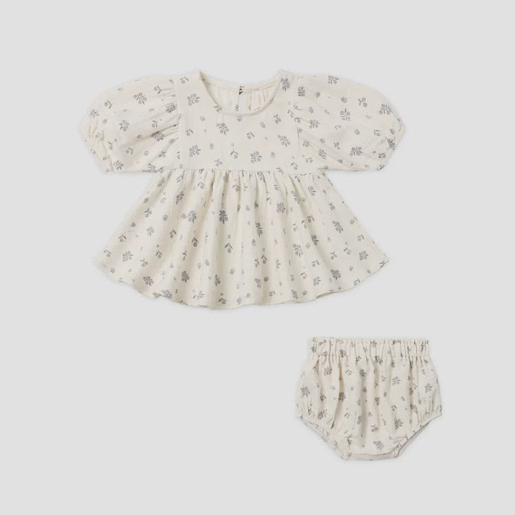A baby girl's two-piece outfit set featuring a short-sleeve puff-sleeve top and matching bloomers, both in a cream-colored cotton fabric with a small gray floral print, shown on a plain light gray background.