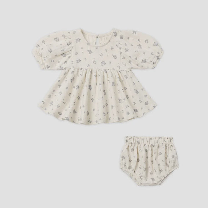 A baby girl's two-piece outfit set featuring a short-sleeve puff-sleeve top and matching bloomers, both in a cream-colored cotton fabric with a small gray floral print, shown on a plain light gray background.