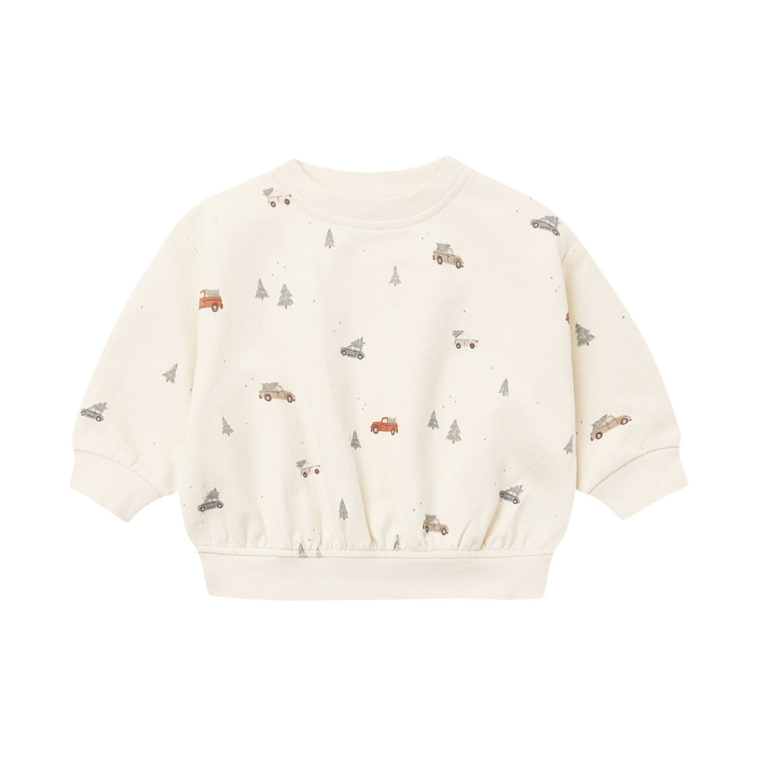 An off-white long-sleeve sweatshirt for toddlers, featuring a playful all-over print of small brown trucks, gray trees, and tiny red accents, displayed on a clean white background.