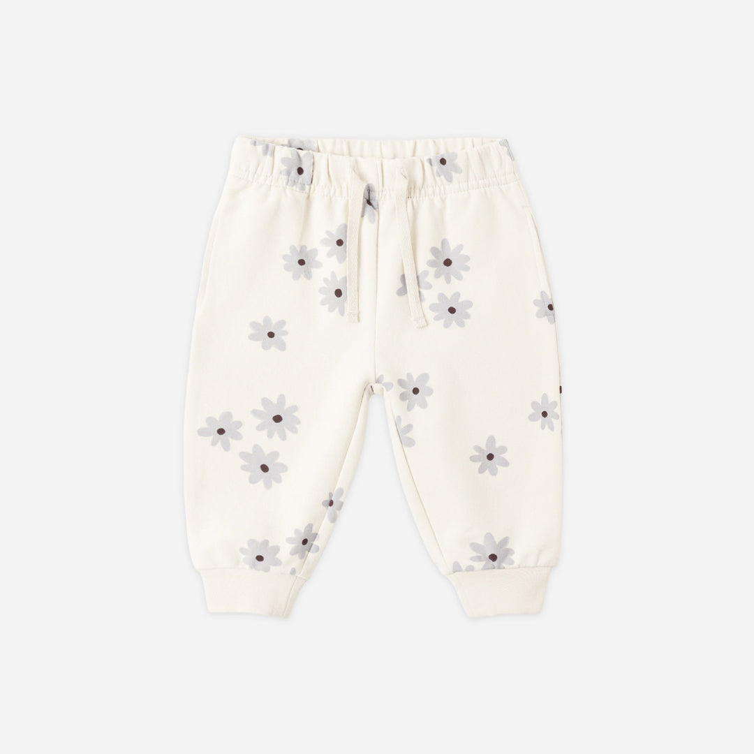 Off-white jogger pants with a small gray and purple daisy print, featuring an elastic waistband with a drawstring and ribbed ankle cuffs, shown flat on a light gray background.