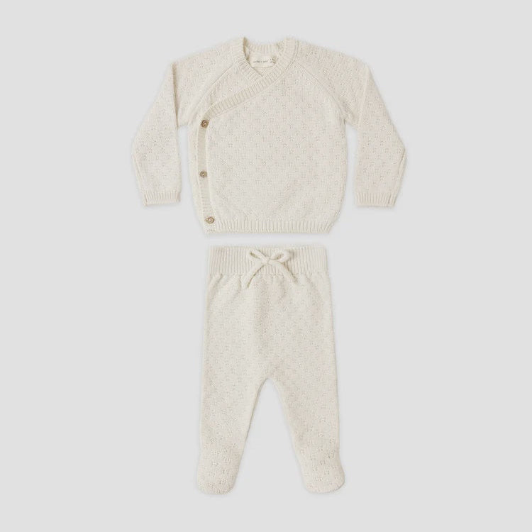 A baby knit two-piece outfit set in cream, featuring a long-sleeve asymmetrical button cardigan and matching footed pants with a drawstring waist, laid flat on a white background.