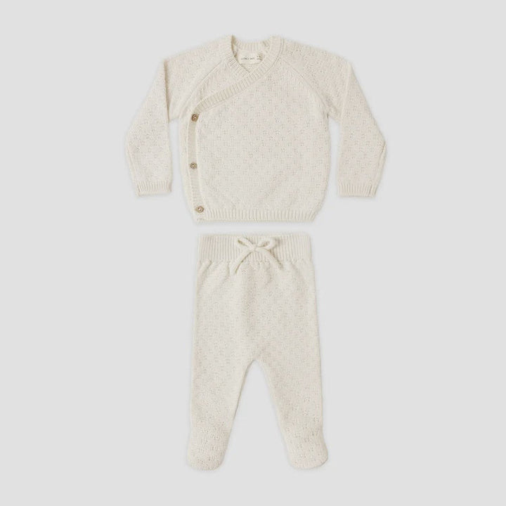 A baby knit two-piece outfit set in cream, featuring a long-sleeve asymmetrical button cardigan and matching footed pants with a drawstring waist, laid flat on a white background.