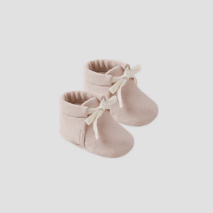 Pair of beige baby booties with white laces on a light gray background