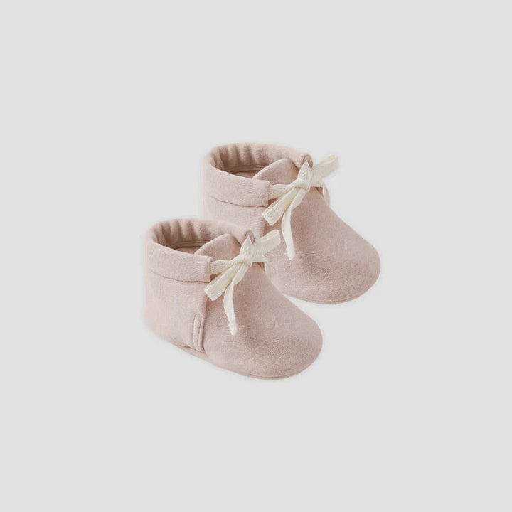 Pair of beige baby booties with white laces on a light gray background