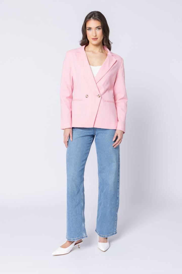 Woman wearing a pink blazer and blue jeans on a white background