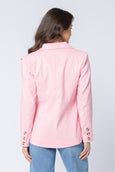 Woman wearing a pink seeing lola blazer with gold buttons on a light gray background