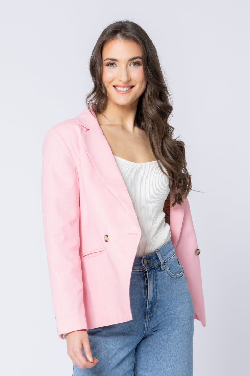 Woman wearing a pink seeking lola blazer over a white top and blue jeans on a light gray background
