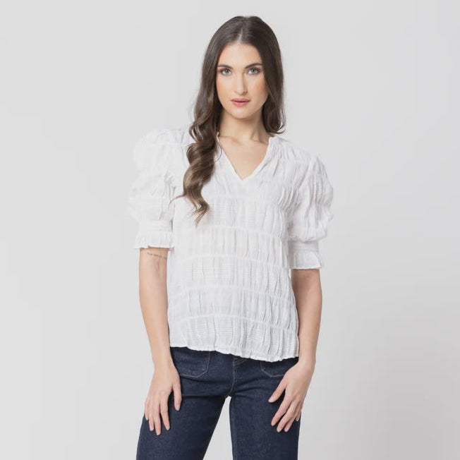 A woman modeling a white short-sleeve blouse with puffed sleeves and dark blue wide-leg jeans against a light gray studio background.