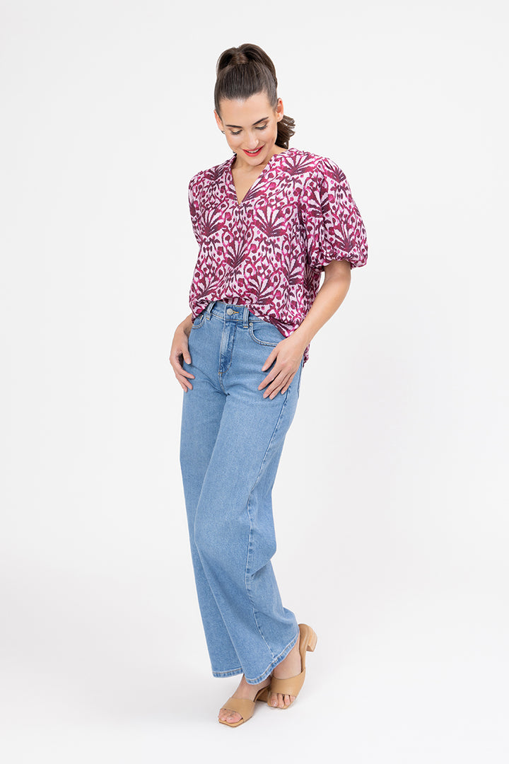 Woman wearing a pink patterned blouse and blue jeans on a white background
