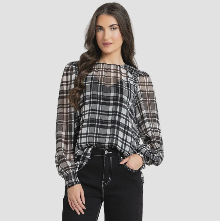 A woman modeling a black, white, and gray plaid long-sleeve blouse with sheer mesh panels, paired with black wide-leg cropped jeans and dark brown heeled sandals, against a solid light gray background.