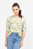 Woman wearing a seeking lola green floral blouse and blue jeans on a white background