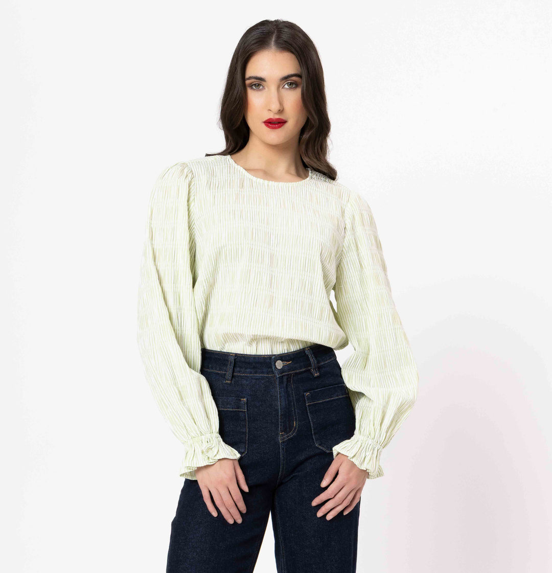 Woman wearing a light green blouse with long sleeves and dark jeans on a white background