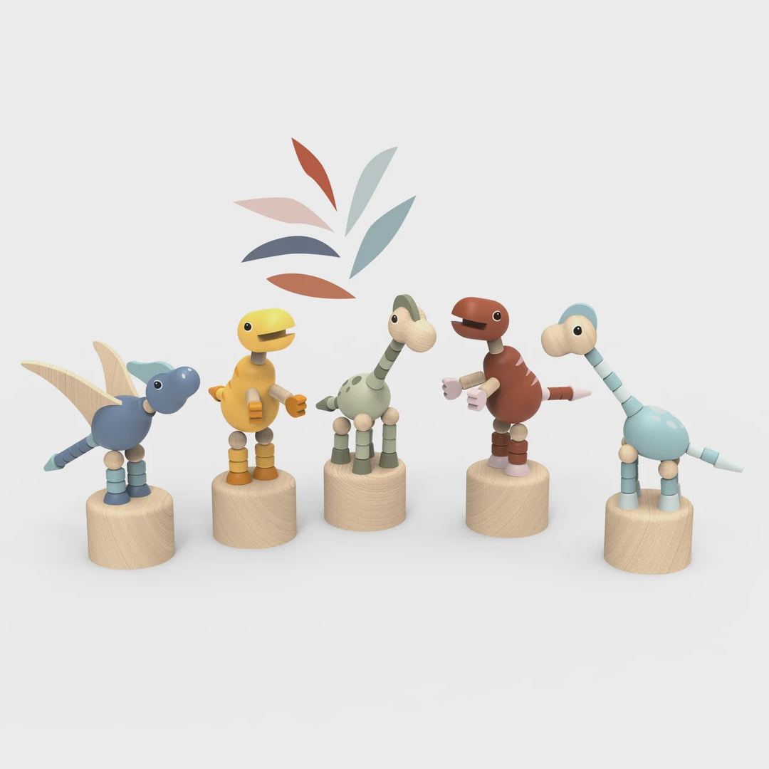 Five wooden dinosaur toy figures in different colors stand on round wooden bases against a light gray background. The toys have smooth painted details and are arranged in a row, with a small abstract leaf-like graphic above them.