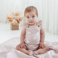Baby wearing a pink floral romper sitting on a white blanket with a soft, blurred background.
