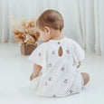 Baby wearing a white outfit with embroidered designs on a light background