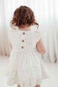 Child wearing a white lace dress with buttons against a white curtain background