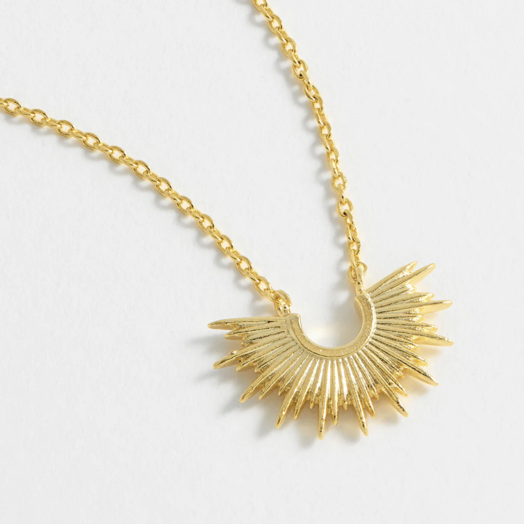 Gold necklace with a sunburst pendant on a light gray background