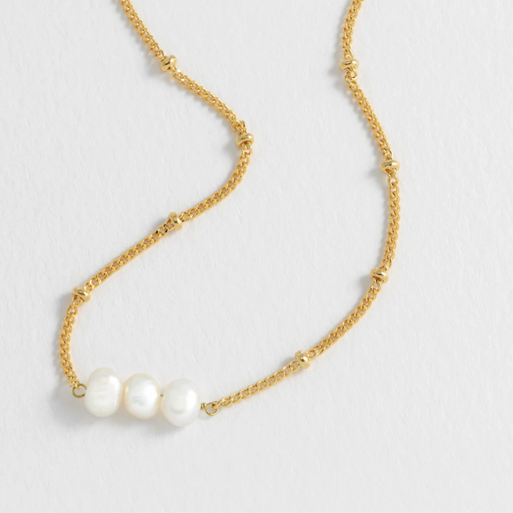 Gold necklace with two pearls on a light gray background