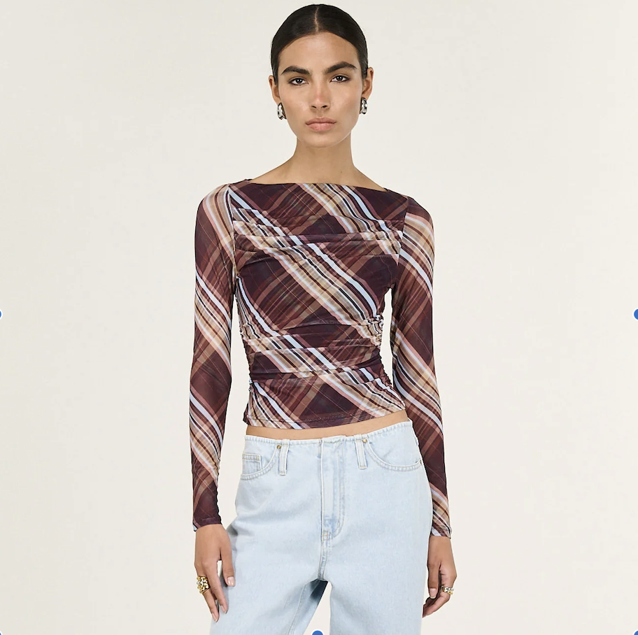 Woman wearing a patterned long-sleeve top and light blue jeans on a white background