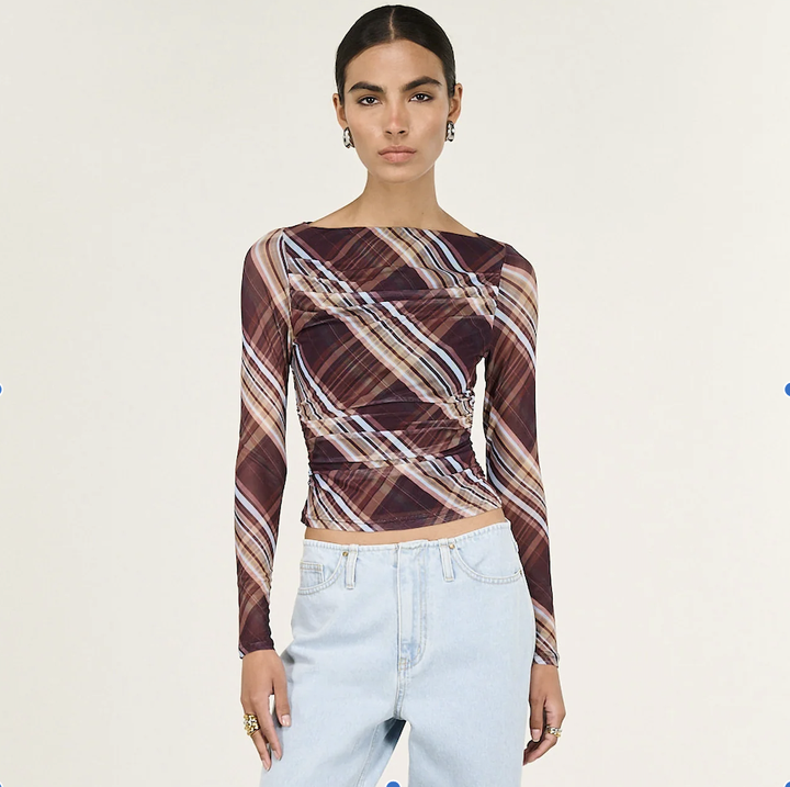 Woman wearing a patterned long-sleeve top and light blue jeans on a white background