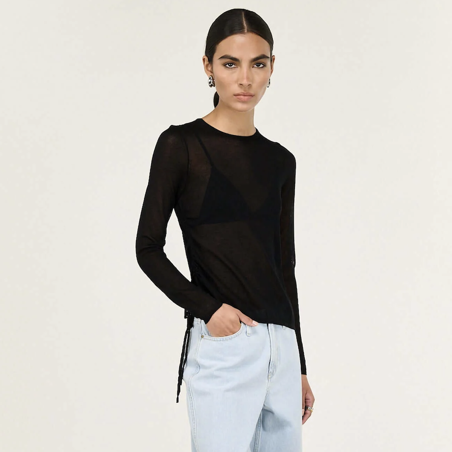 Woman wearing a black long-sleeve top and light blue jeans on a white background