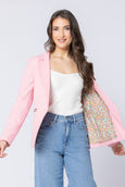 Woman wearing a pink seeking lola blazer over a floral shirt with blue jeans on a light gray background