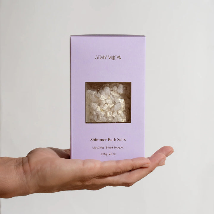 Purple box of Shimmer Bath Salts held in a hand against a light gray background
