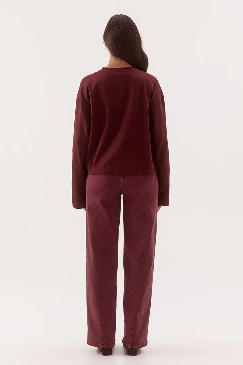 A woman viewed from the back wearing a matching burgundy long-sleeve top and wide-leg pants set against a plain white studio background.